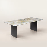 Natural green marble dining table with grey titanium-finish stainless steel double pedestal base, angled view in a showroom.